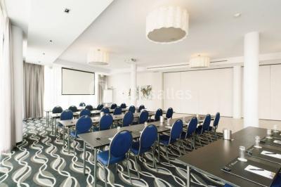 Salle de réunion moderne avec table rectangulaire, chaises noires, écran mural, tableau blanc et minibar.