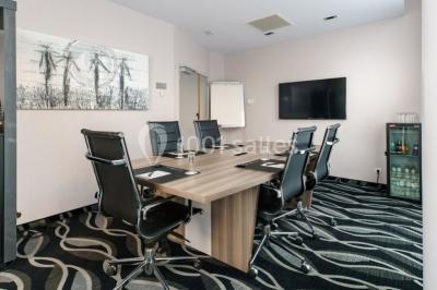 Salle de réunion moderne avec table rectangulaire, chaises noires, écran mural, tableau blanc et minibar.
