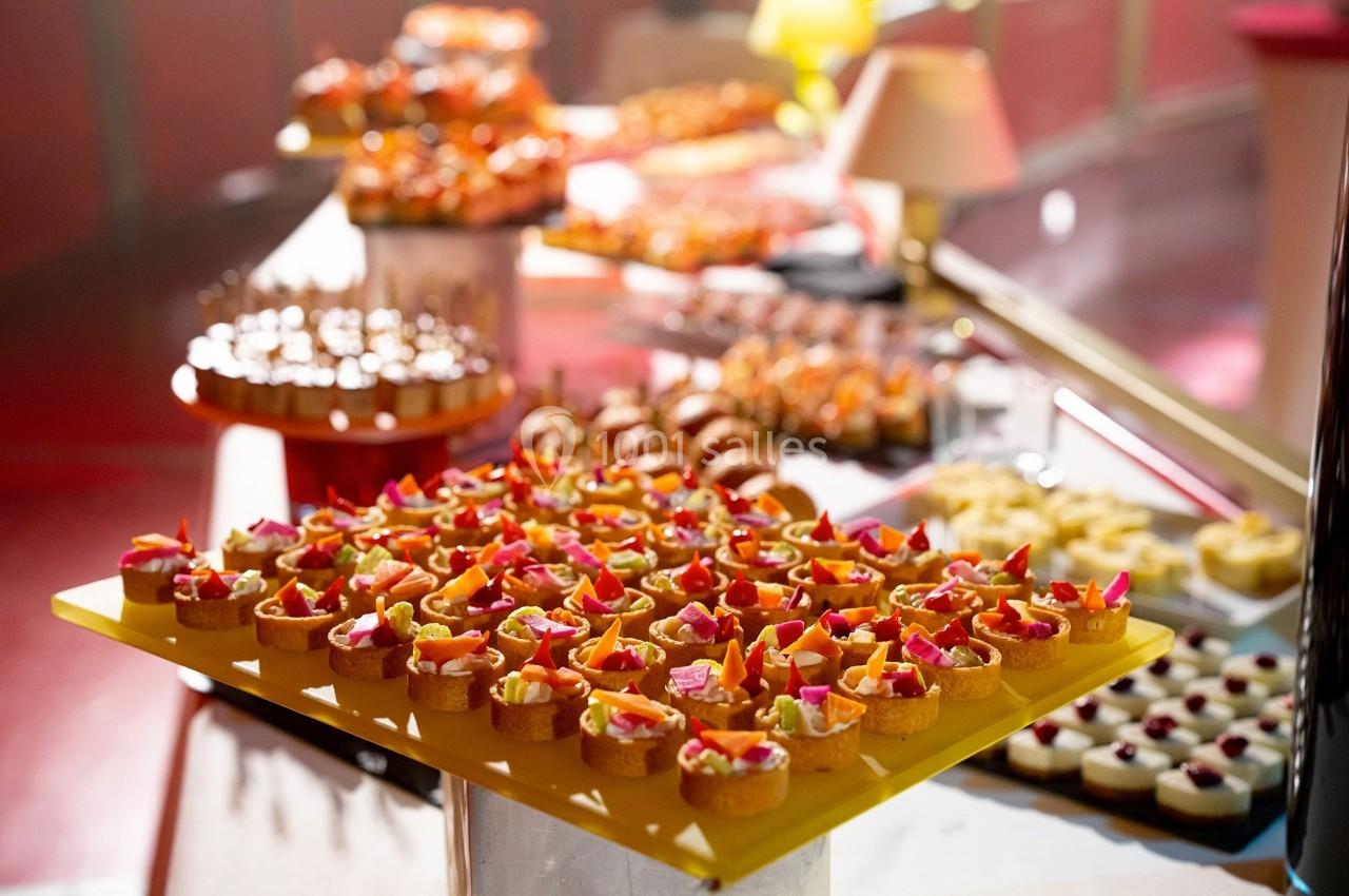 Plateau de petits fours variés disposés sur une table, entouré d'autres desserts dans un cadre lumineux.