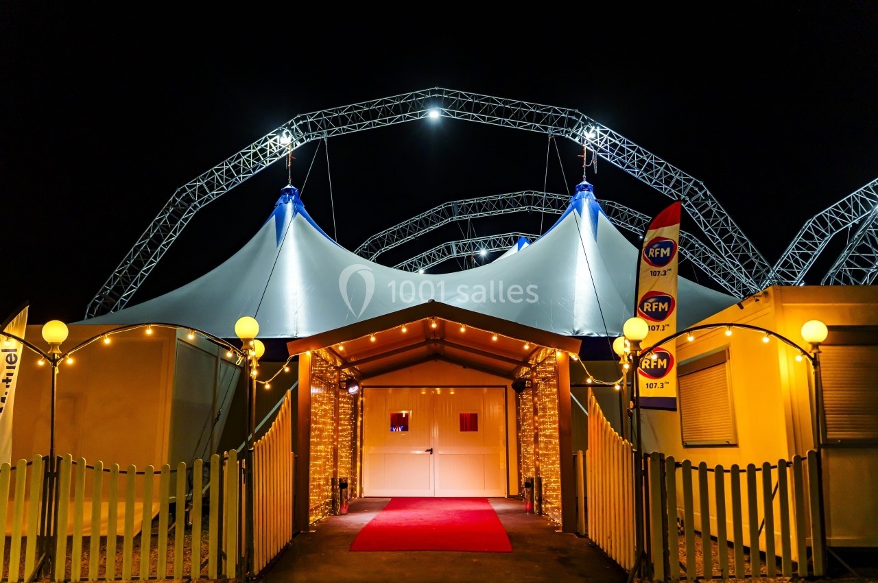 Location salle Vaulx-en-Velin (Rhône) - Cirque Imagine #1 Entrée d’un chapiteau illuminé la nuit, avec tapis rouge, guirlandes lumineuses et structures métalliques visibles.