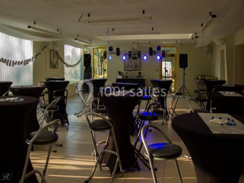 Salle de réception décorée avec des tables hautes noires, des chaises et un éclairage de scène en arrière-plan.