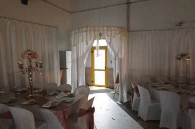 Salle vide avec parquet, murs clairs, table en métal, miroir mural et lumière naturelle entrant par une fenêtre.