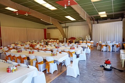 Salle vide avec parquet, murs clairs, table en métal, miroir mural et lumière naturelle entrant par une fenêtre.
