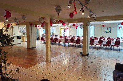 Salle vide avec parquet, murs clairs, table en métal, miroir mural et lumière naturelle entrant par une fenêtre.