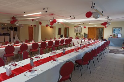 Salle vide avec parquet, murs clairs, table en métal, miroir mural et lumière naturelle entrant par une fenêtre.