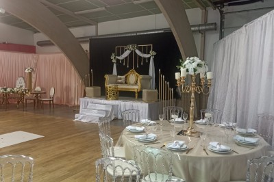 Salle vide avec parquet, murs clairs, table en métal, miroir mural et lumière naturelle entrant par une fenêtre.