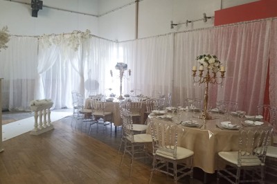 Salle vide avec parquet, murs clairs, table en métal, miroir mural et lumière naturelle entrant par une fenêtre.