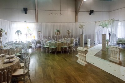 Salle vide avec parquet, murs clairs, table en métal, miroir mural et lumière naturelle entrant par une fenêtre.
