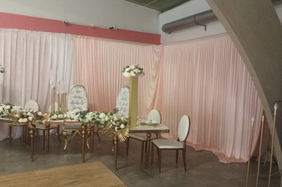 Salle vide avec parquet, murs clairs, table en métal, miroir mural et lumière naturelle entrant par une fenêtre.