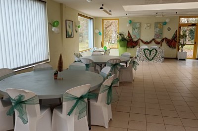 Salle vide avec parquet, murs clairs, table en métal, miroir mural et lumière naturelle entrant par une fenêtre.