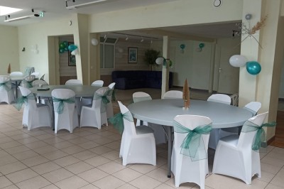Salle vide avec parquet, murs clairs, table en métal, miroir mural et lumière naturelle entrant par une fenêtre.