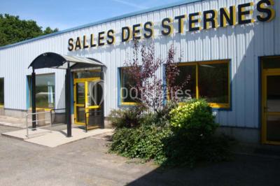 Salle lumineuse avec une table en métal, des fenêtres et une porte jaune donnant sur l'extérieur.
