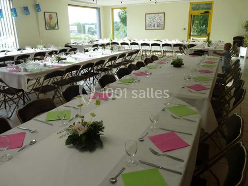 Salle décorée pour un événement, avec de longues tables couvertes de nappes blanches, serviettes roses et vertes.