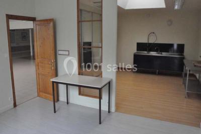 Salle lumineuse avec une table en métal, des fenêtres et une porte jaune donnant sur l'extérieur.