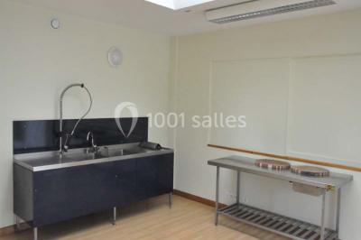 Salle lumineuse avec une table en métal, des fenêtres et une porte jaune donnant sur l'extérieur.