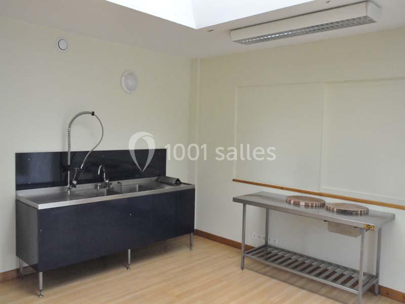 Évier professionnel avec douchette et plan de travail en acier inoxydable dans une pièce lumineuse au sol en bois.