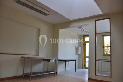 Salle lumineuse avec une table en métal, des fenêtres et une porte jaune donnant sur l'extérieur.