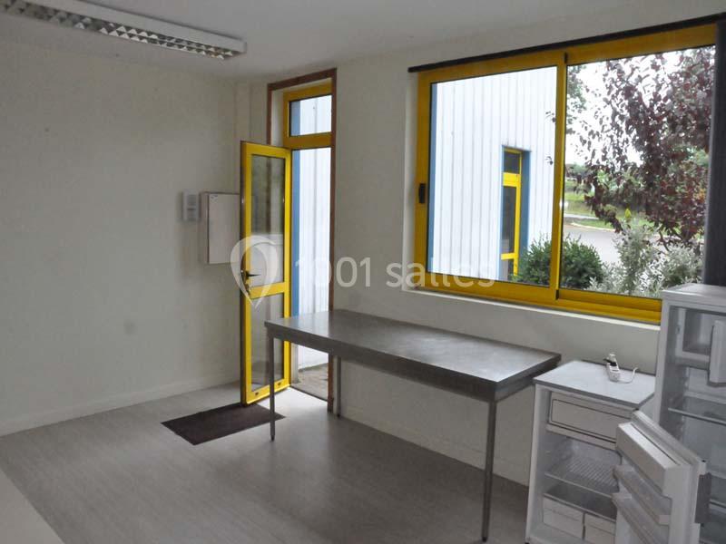 Salle lumineuse avec une table en métal, des fenêtres et une porte jaune donnant sur l'extérieur.