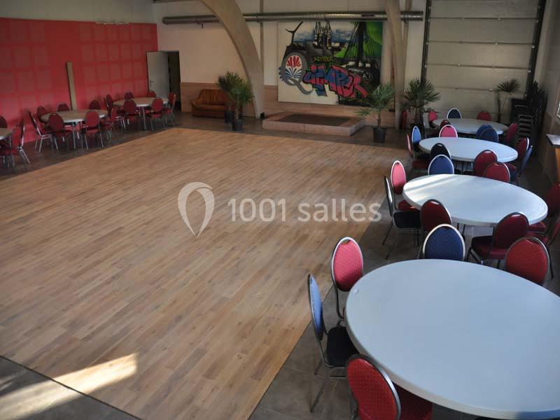 Salle spacieuse avec parquet central, tables rondes et chaises colorées, mur décoré d'une fresque en arrière-plan.