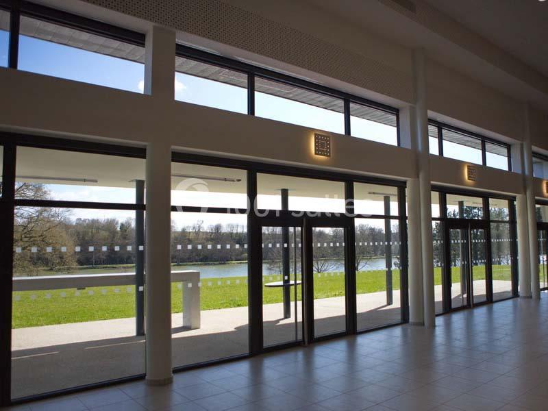 Baie vitrée donnant sur une terrasse et un paysage verdoyant avec un lac en arrière-plan.