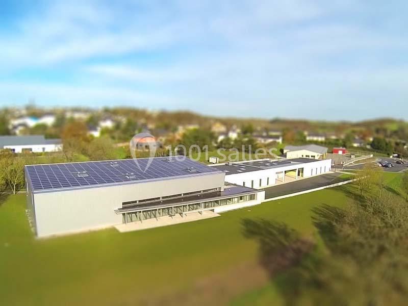 Bâtiment moderne avec panneaux solaires sur le toit, entouré d'espaces verts et situé dans un environnement semi-urbain.