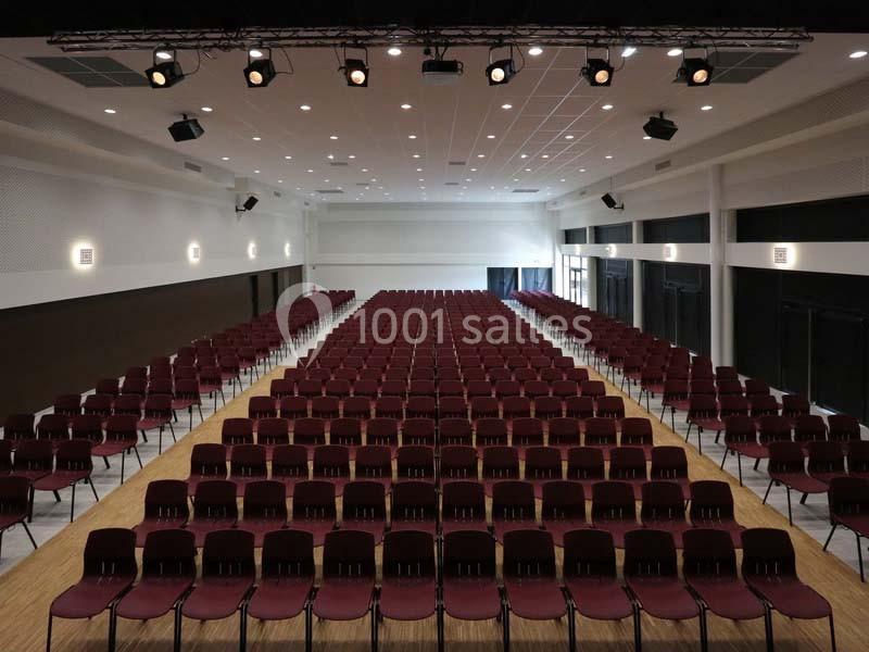 Salle de conférence vide avec rangées de chaises rouges alignées et éclairage au plafond.
