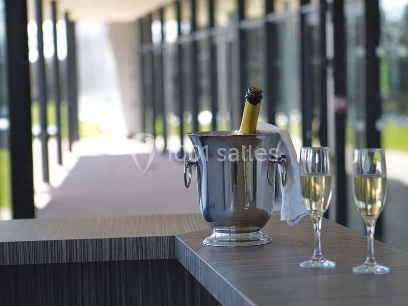 Seau à champagne avec bouteille et deux verres remplis sur un comptoir, dans un espace lumineux avec baies vitrées.