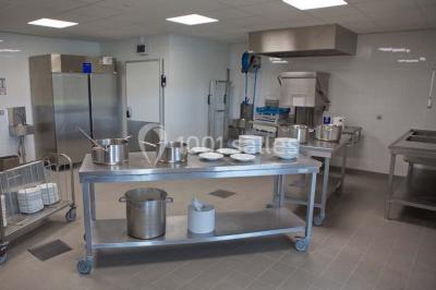 Cuisine professionnelle avec plans de travail en inox, casseroles, assiettes empilées et équipements de restauration.