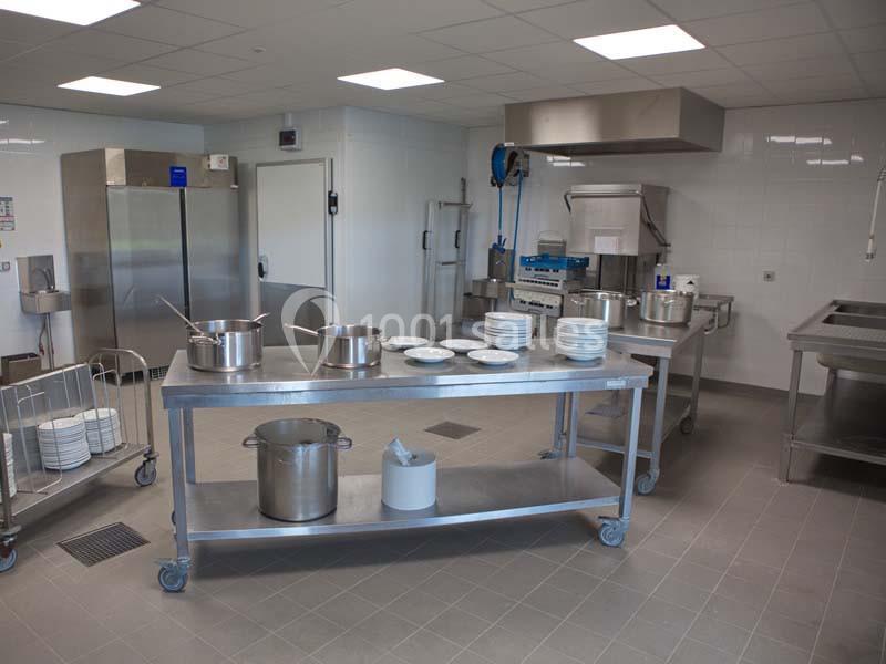 Cuisine professionnelle avec plans de travail en inox, casseroles, assiettes empilées et équipements de restauration.