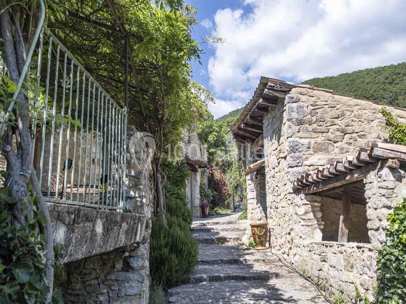 Ruelle pavée bordée de maisons en pierre, entourée de végétation et baignée de lumière naturelle.