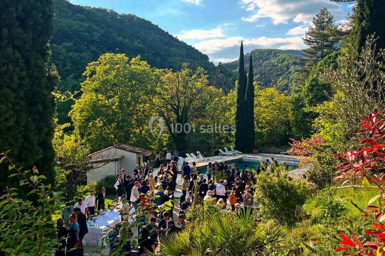 Groupe de personnes rassemblées dans un jardin verdoyant près d'une piscine, entouré de collines boisées.