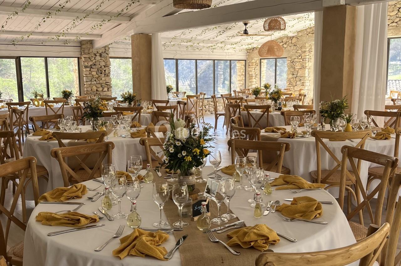Salle de réception décorée avec des tables rondes, nappes blanches, serviettes jaunes et arrangements floraux.