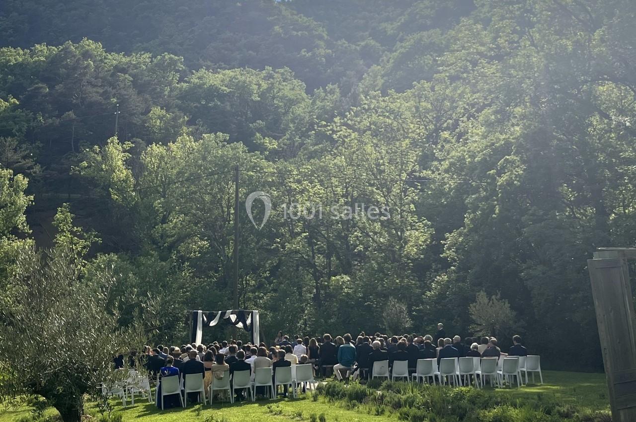 Cérémonie en plein air avec des invités assis, entourée de verdure et de collines sous un ciel ensoleillé.
