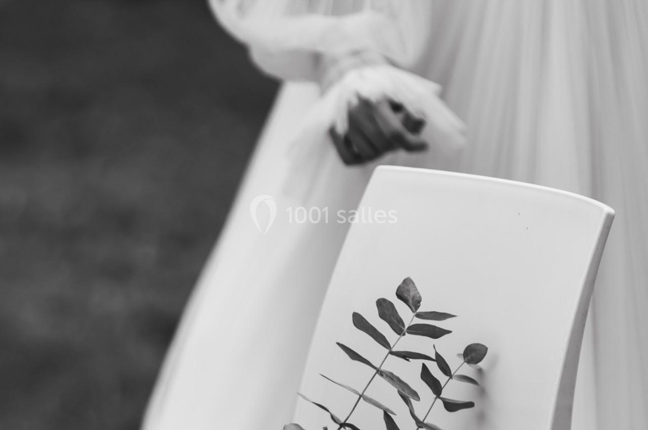 Une chaise blanche avec un bouquet de fleurs posé dessus, en arrière-plan une personne en robe claire floue.