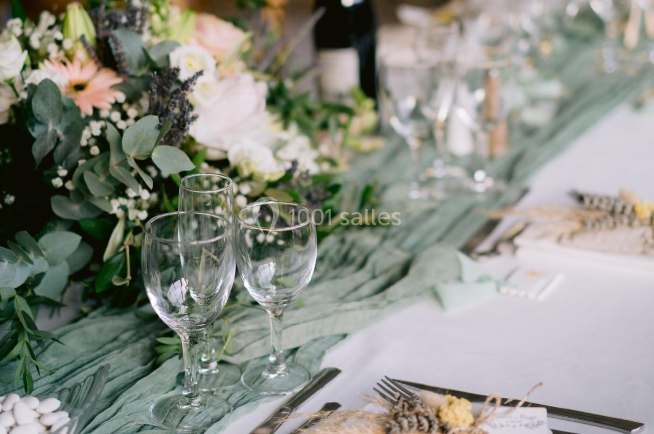 Table décorée pour un repas avec nappes blanches, verres, couverts, fleurs et éléments naturels.