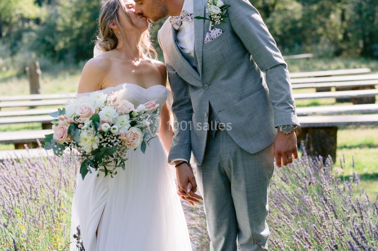 Un couple de mariés s'embrasse dans un jardin entouré de lavandes sous une lumière naturelle.