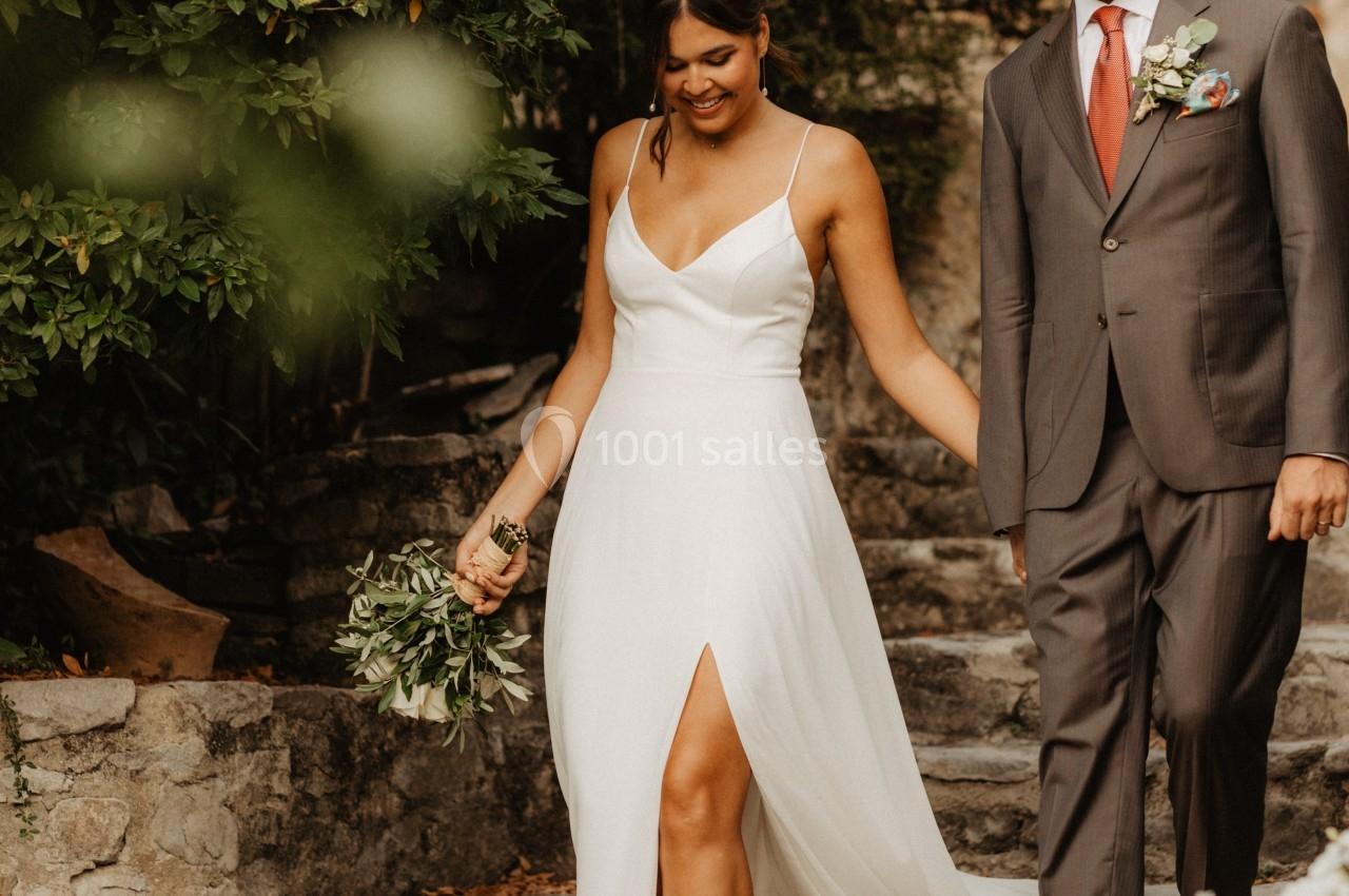 Un couple souriant descend des marches en pierre, la femme en robe blanche et l'homme en costume gris.
