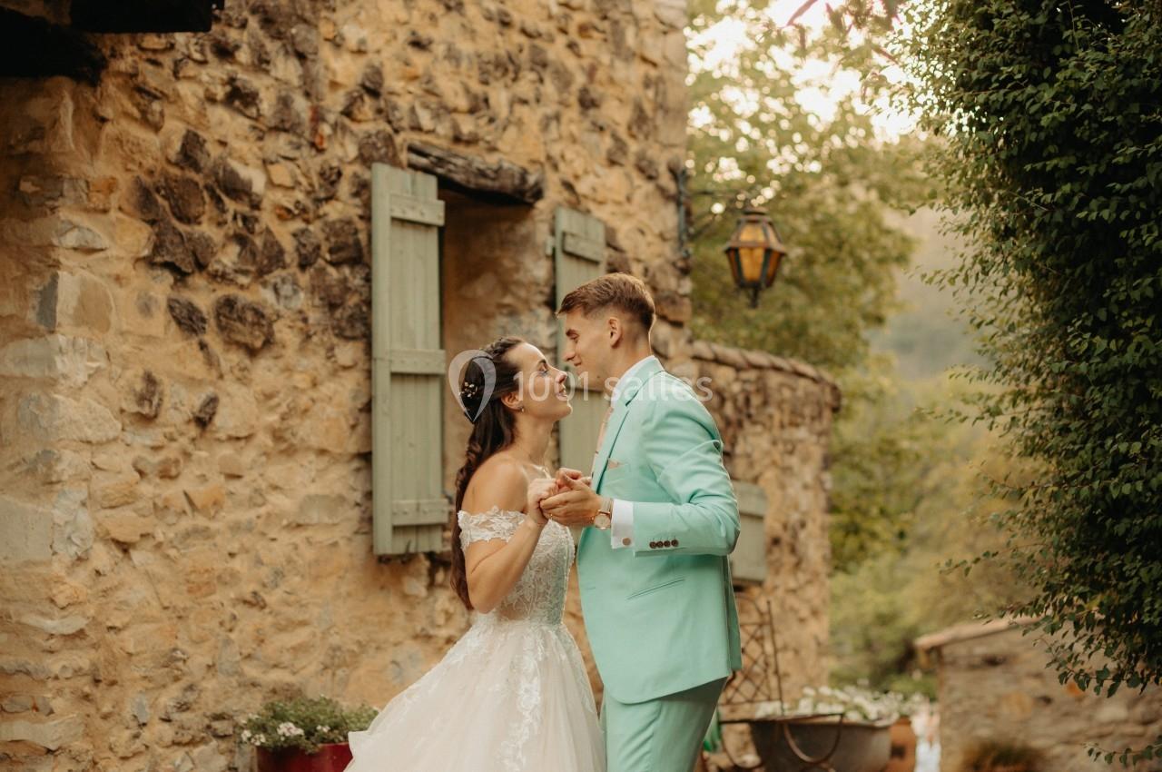 Un couple en tenue de mariage danse dans une ruelle pavée bordée de murs en pierre et de verdure.