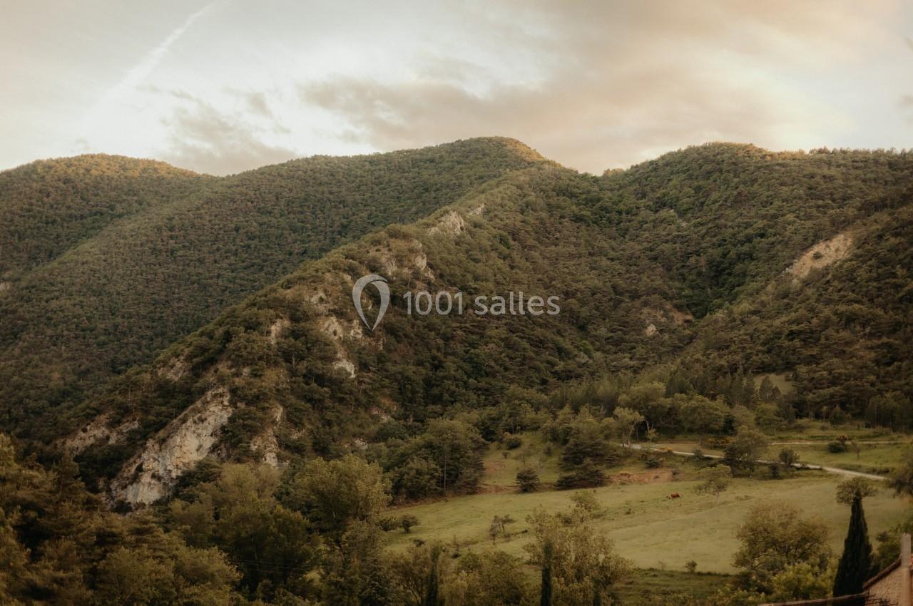 Paysage de collines verdoyantes au coucher du soleil, avec des prairies et des arbres au premier plan.