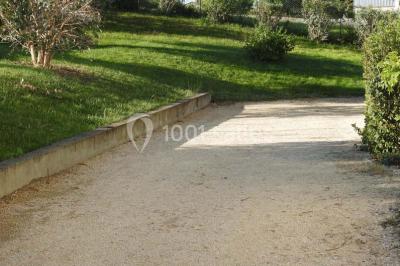 Allée en gravier bordée de pelouse et d'arbustes, menant vers un espace verdoyant.