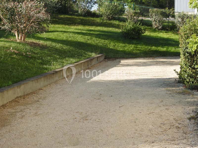 Allée en gravier bordée de pelouse et d'arbustes, menant vers un espace verdoyant.