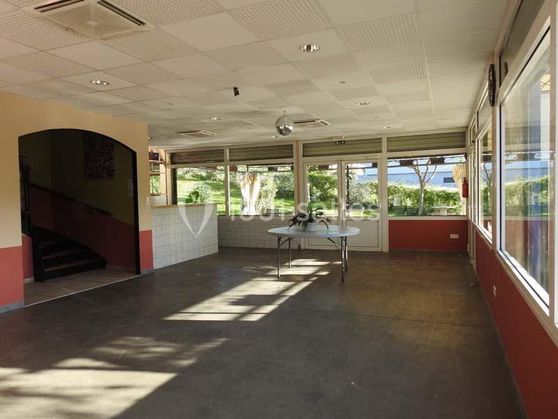Salle lumineuse avec grandes baies vitrées donnant sur un espace vert, table centrale et escalier sur la gauche.