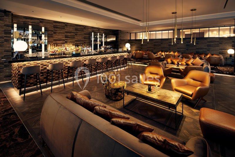 Bar moderne avec comptoir en pierre, tabourets hauts, fauteuils en cuir et éclairage tamisé dans une ambiance chaleureuse.