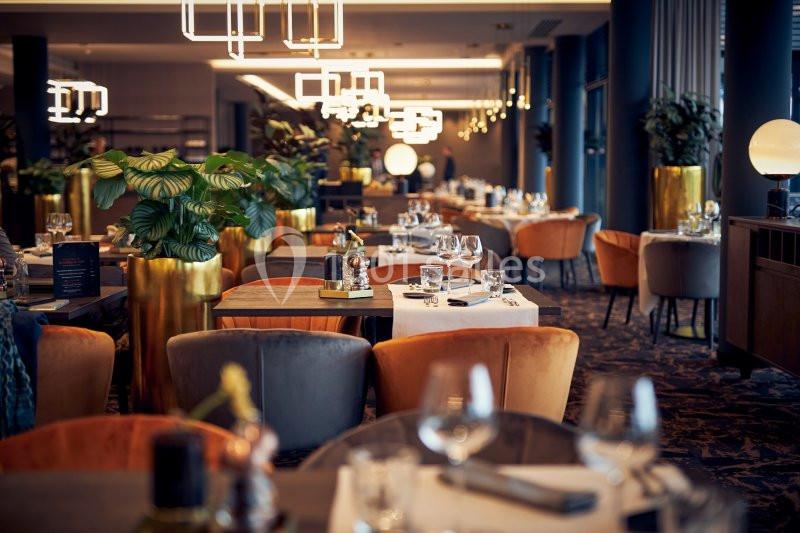 Salle de restaurant élégante avec tables dressées, chaises colorées et plantes décoratives dans un éclairage chaleureux.