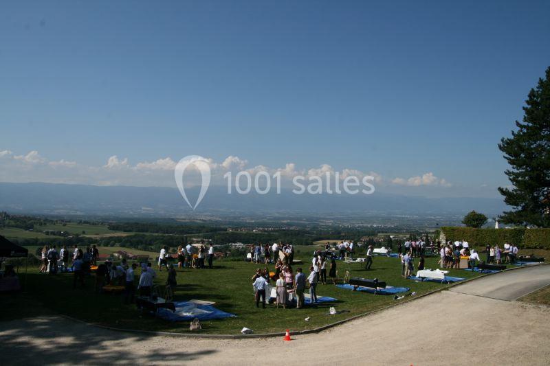 Groupe de personnes rassemblées sur une pelouse avec vue panoramique sur une vallée et des montagnes au loin.