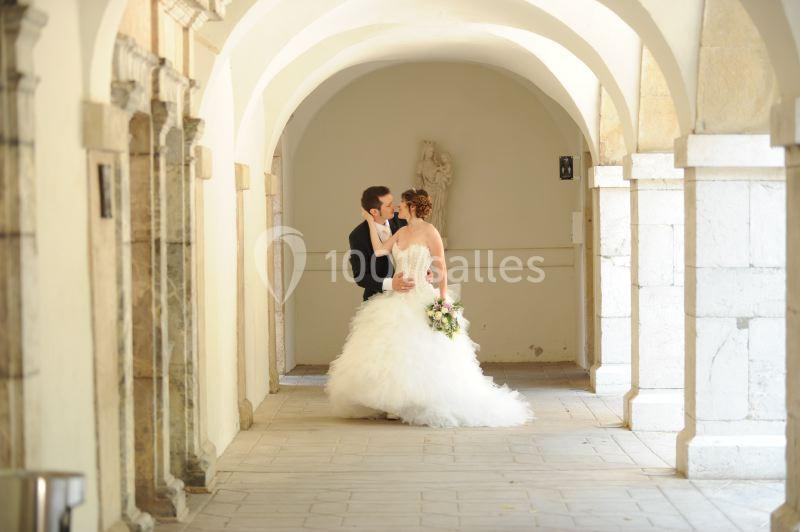 Un couple de mariés échange un moment tendre dans une galerie lumineuse aux arches en pierre.
