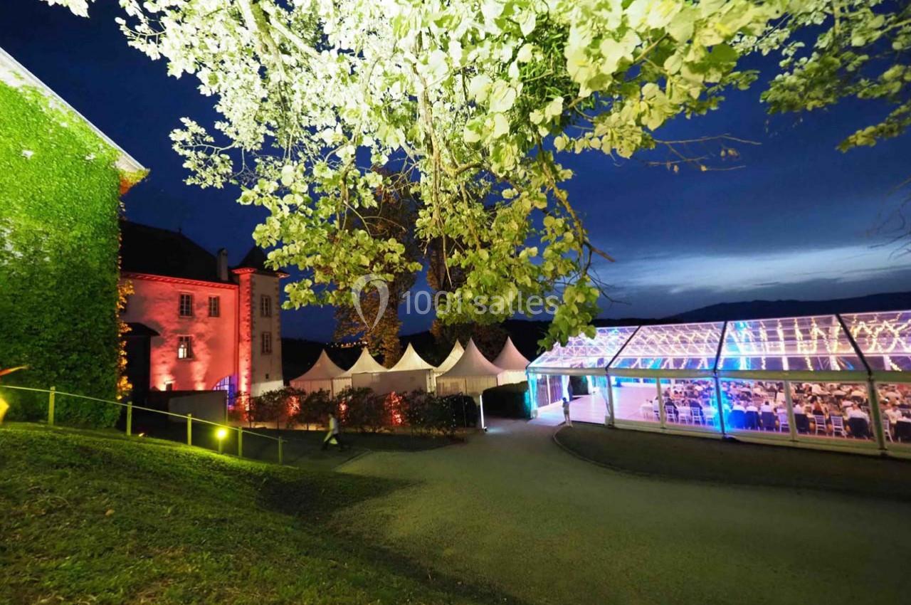 Allée éclairée menant à un bâtiment illuminé et une tente transparente accueillant un événement nocturne.