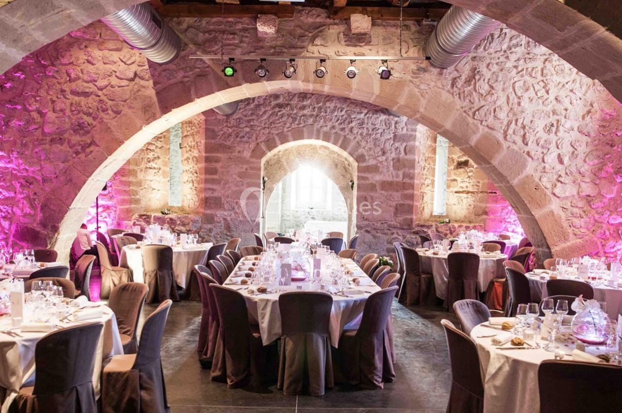 Salle voûtée en pierre avec des tables rondes élégamment dressées pour un événement ou un banquet.