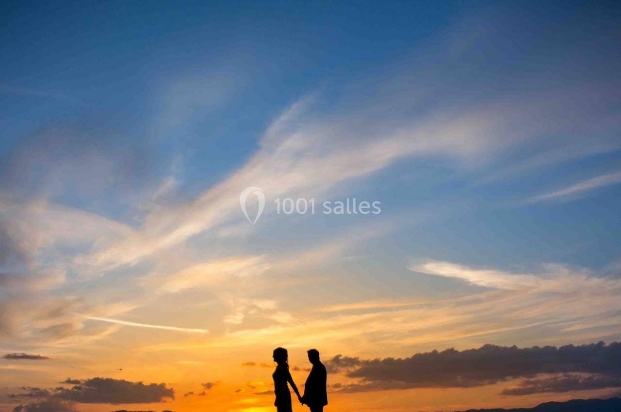 Deux silhouettes se tenant la main devant un ciel coloré par un coucher de soleil.