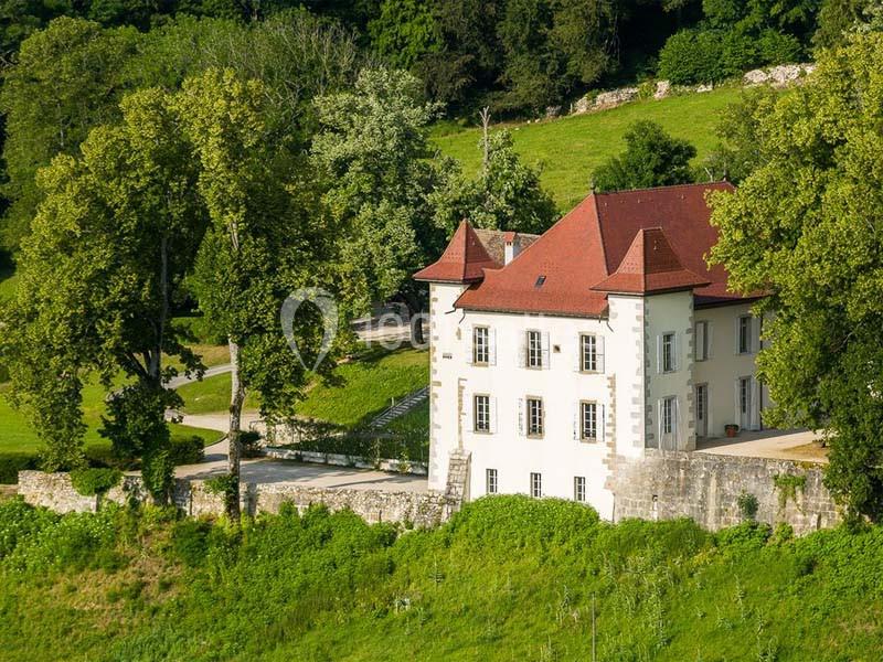 Manoir blanc avec toit rouge entouré de verdure et d'arbres, situé dans un paysage rural ensoleillé.
